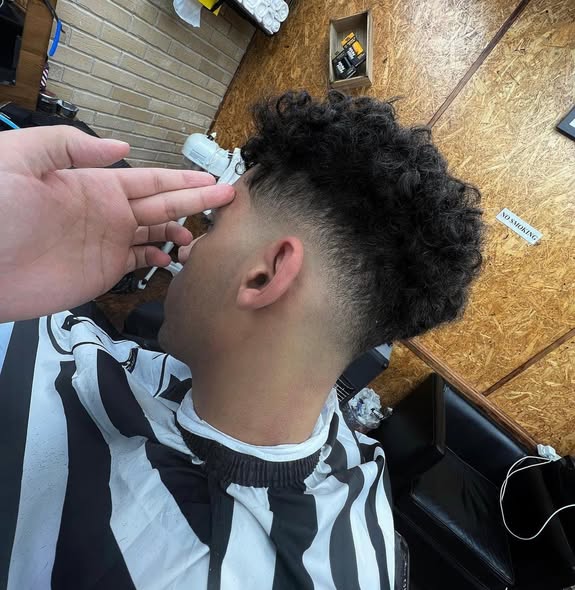 Curly top with a low taper fade being checked by the barber