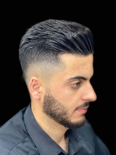 Slick-back pompadour with a skin fade and a shaped beard, side profile